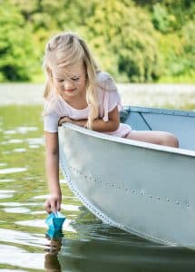 young girl launching paper boat into water