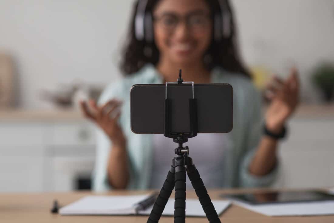 cell phone on tripod with woman shown behind camera recording video