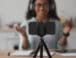 cell phone on tripod with woman shown behind camera recording video